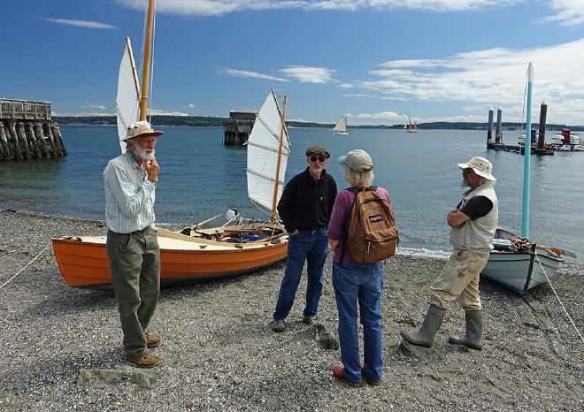 Four people standing on the beach in front of a junk rigged boat